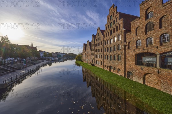 Historic salt warehouses, river Trave, blue sky with veil clouds in the backlight of the sun,
