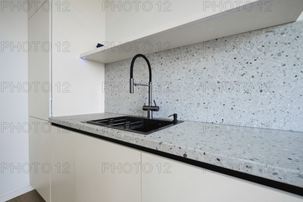 A sleek kitchen area showcases a minimalist design with a modern countertop and stylish black sink.