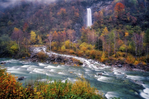 Waterfall with Verzasca river surrounded by autumn coloured deciduous trees, rainy and foggy