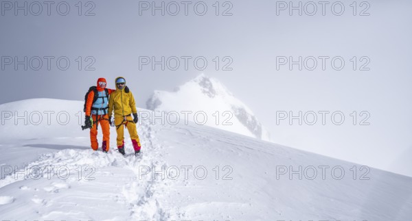 Two ski tourers on the summit of the Wildhorn, Snowy mountain landscape and fog, Bernese Alps,