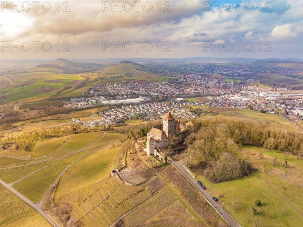 A castle stands above the fields and the village, surrounded by picturesque hills under a cloudy