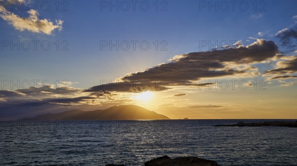 Dramatic sunset over the sea with clouds and island on the horizon, rays in the sky, sunset,