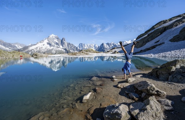 Young man doing a handstand, in front of mountain landscape with mountain lake, tourist at Lac