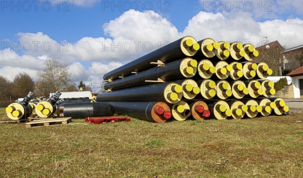 Stacked district heating pipes with yellow ends lie piled up in a meadow