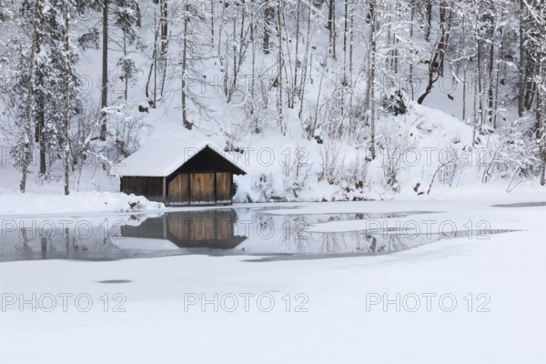 Snow covered boat shelter on Lake Almsee which is partly frozen and snow covered. Snow on the