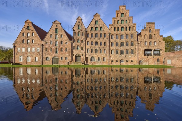 Historic salt warehouses with reflections on the water surface of the Trave, blue sky with veil