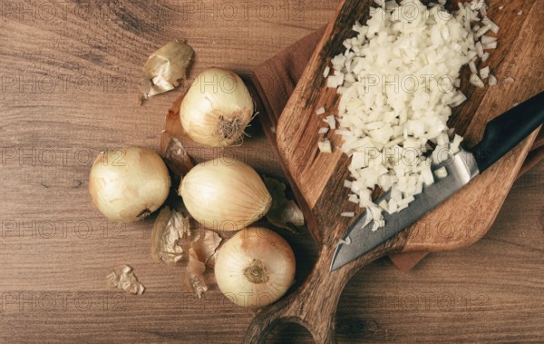 Finely chopped onion on a chopping board with a knife, wooden table, top view, no people