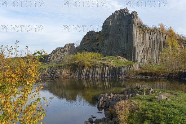 Impressive basalt columns are reflected in a quiet pond in autumnal surroundings, manor house