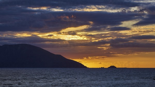 Sunset over the sea with dark clouds and silhouette of the mountains on the horizon, sunset,