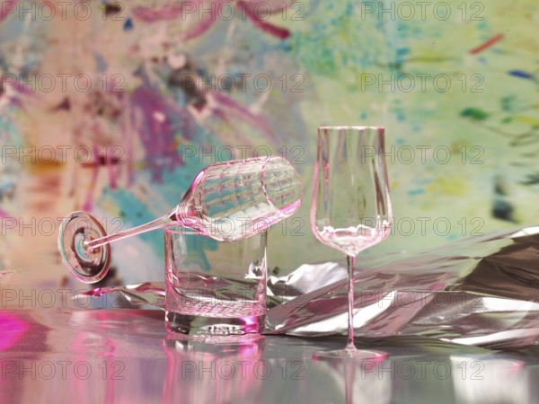 Various glasses on silver foil, behind them various splashes of colour, studio shot