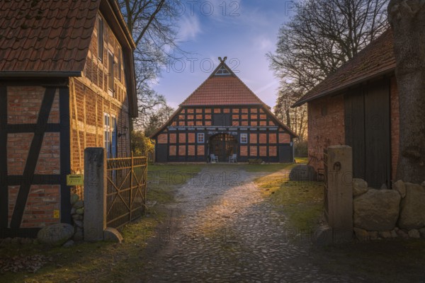 View of a courtyard entrance with a half-timbered farmhouse behind it in the evening light,