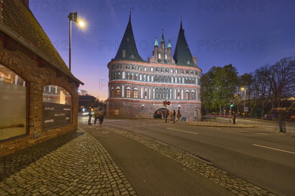 City gate Lübeck Holstentor, historic brick building, footpath and cycle path, evening blue hour,