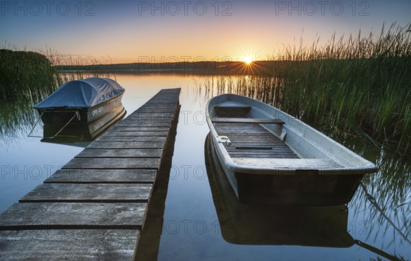 Quiet lake at sunset, rowing boats moored in the water at a wooden jetty, Gudelacksee, Lindow,
