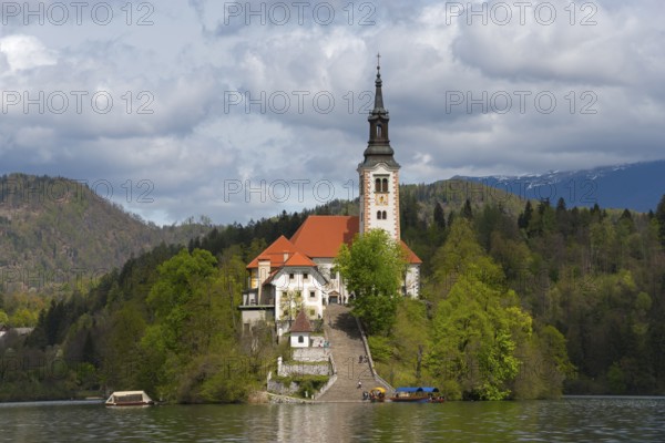Church on a green island in the lake, framed by wooded mountains, Bled Island with St Mary's