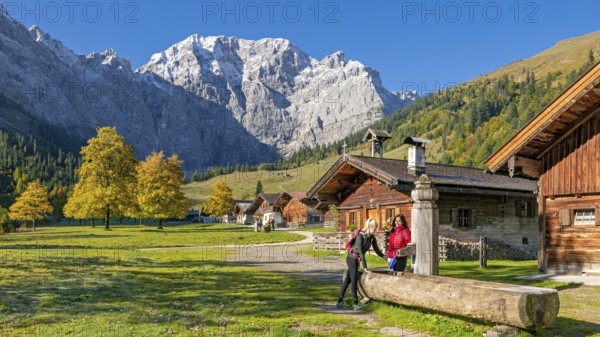 The alpine village of Eng in autumn, two hikers fill a water bottle at the wooden fountain,