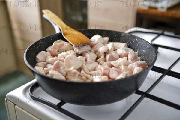 Cooking chunks of chicken in a black skillet over a gas stovetop. The cozy kitchen environment