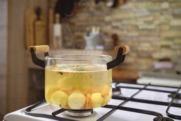 A clear pot filled with simmering vegetable broth sits on a gas stove, showcasing vibrant