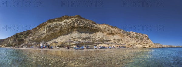 Rocky coastal landscape with Paralia Agios Theodoros sandy beach and sunshades in front of a clear