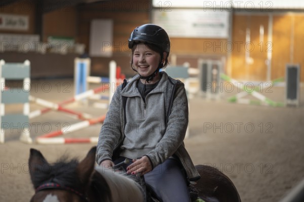 Laughing little girl, 10 years old, on a horse in an indoor riding arena, Mecklenburg-Vorpommern,