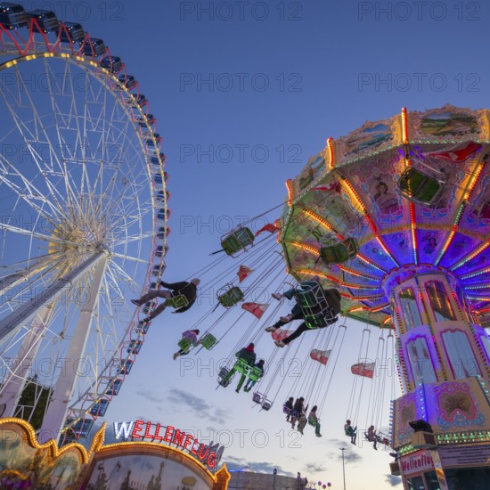A funfair at dusk with illuminated chain carousel and Ferris wheel, Europa Rad, rides, wave flight,