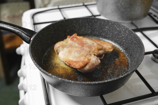 Juicy turkey meat sizzles in a black skillet placed on a gas stove in a cozy kitchen. The cooking
