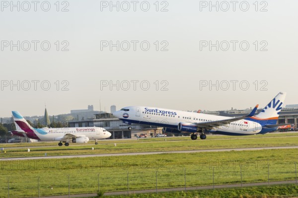 Two SunExpress and Eurowings aeroplanes at an airport. One takes off and the other approaches,