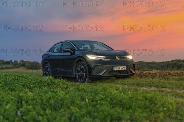 A car stands in front of a dramatic sunset in a field with a colourful sky, electric car, VW ID5,