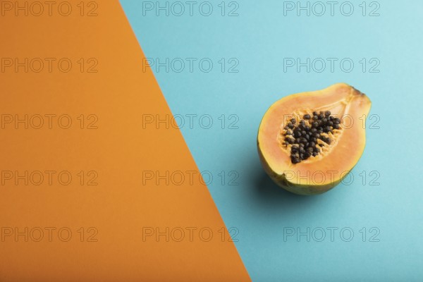 Ripe cut papaya on orange and blue pastel background. Side view, copy space. Tropical, healthy