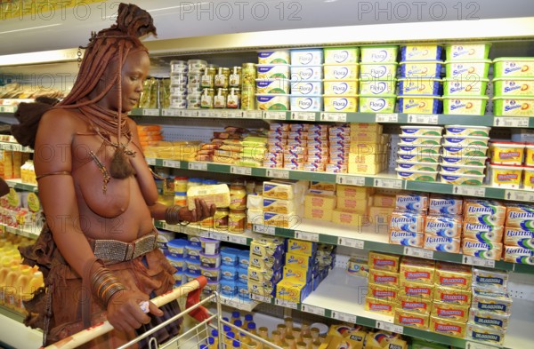 Traditionally dressed Himba woman holding a packet of butter, standing in front of the refrigerated