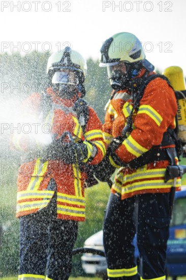 Two firefighters in full protective clothing spraying water with a fire hose, fire brigade,