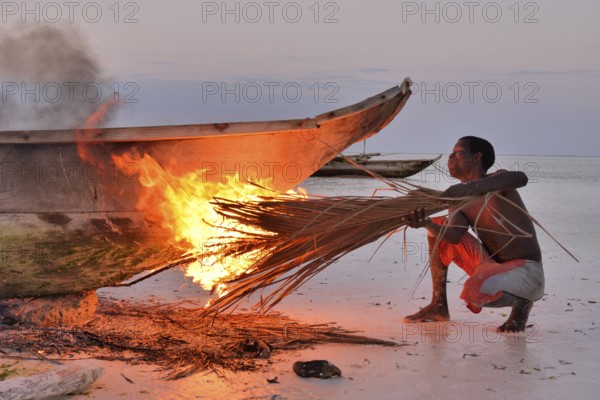 Fisherman smoking his boat with burning palm fronds, to harden the surface and to remove vermin,