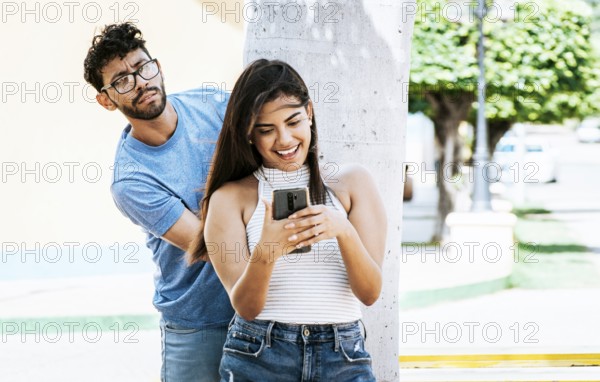 Jealous boyfriend spying on his girlfriend's cell phone in the park, Jealous man spying on his
