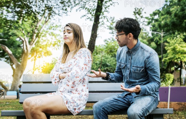 Man arguing with his girlfriend sitting in a park. Upset couple arguing in a park. A young couple