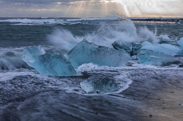 Waves breaking on icebergs on the black beach of Breidamerkursandur, near Jökullsarlon, Sudurland,