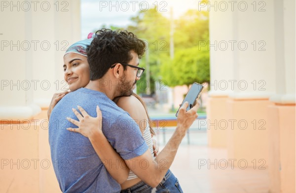 Unfaithful boyfriend hugging his girlfriend and looking at the cell phone. Concept of unfaithful