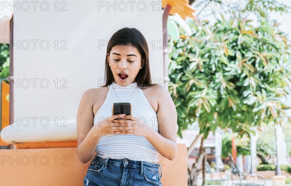 Surprised person looking at cell phone outdoor. Girl with cell phone with a surprised face leaning