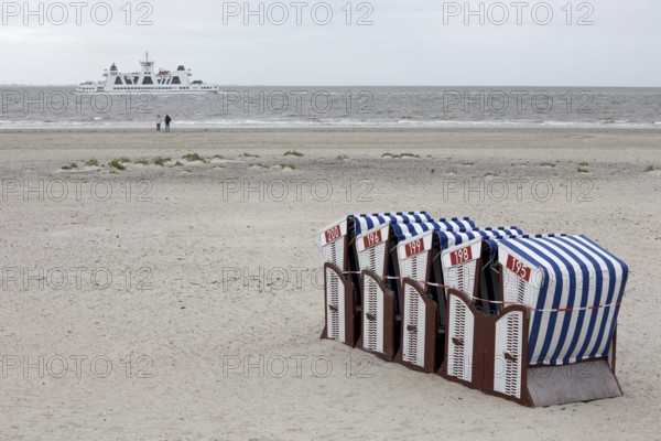 Beach chairs tied together on the beach with only two people on the water and ferry departing, end