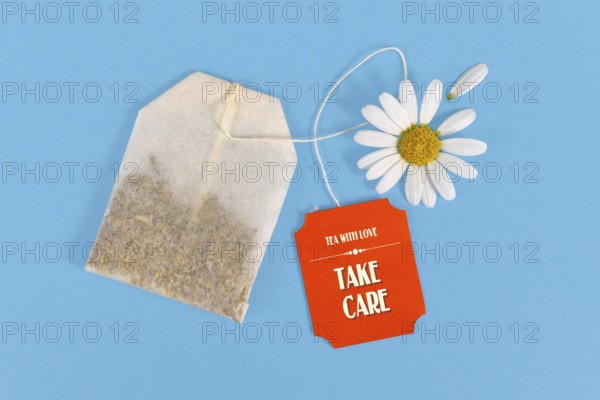 Tea bag with made up cute red label with text Take care with daisy flower on blue background