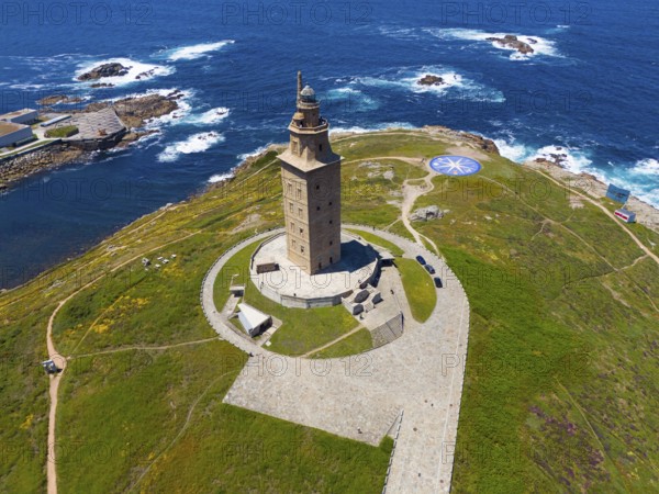 Majestic lighthouse on the coast with green grass and deep blue sea under a bright blue sky, aerial