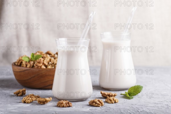 Organic non dairy walnut milk in glass and wooden plate with walnuts on a gray concrete background.
