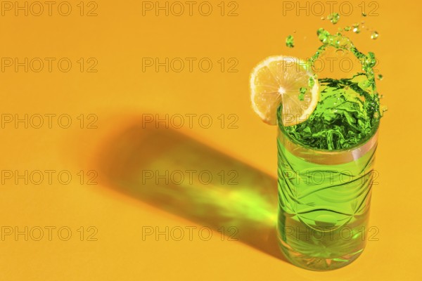 A green, sparkling cocktail with a slice of lemon casts shadows on an orange background