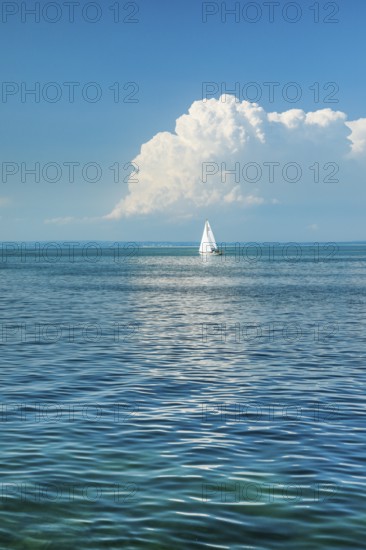 White sailboat on the turquoise water of Lake Constance with a low, large spring cloud in the