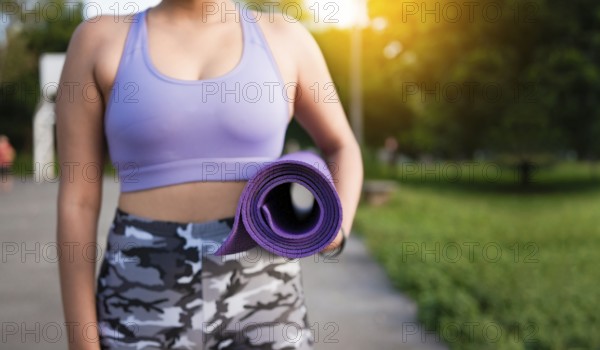 Unrecognizable woman holding a mat in the park. Athlete woman's hands carrying the mat after