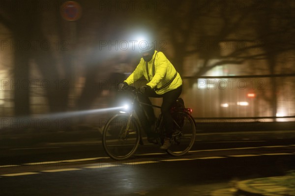 Cyclist with 2 lights and yellow cycling jacket, luminous, inner city traffic, fog, autumn, winter,