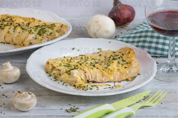 Savoury strudel with cheese and ham on a plate, alongside cutlery and a glass of red wine