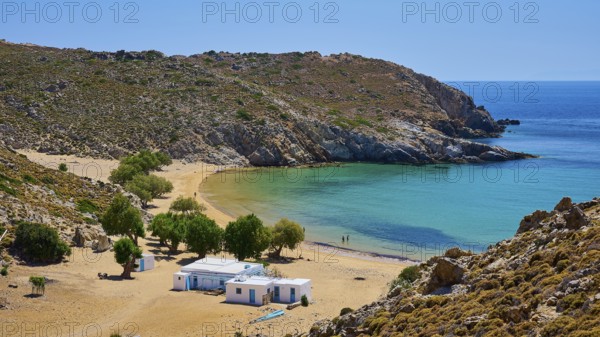 Secluded bay with clear water and golden sand, houses and trees, embedded in a rocky landscape