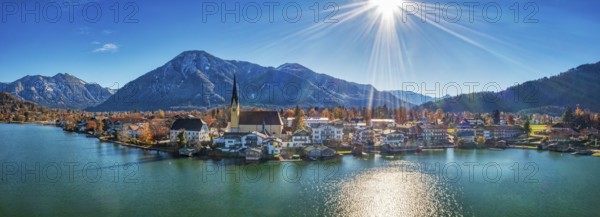 Panoramic shot of a village on the lake with mountains in the background, the sun shines on a clear