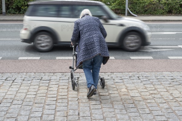 Elderly woman with rollator wants to cross the road, in front of her a passing car, Erlangen,