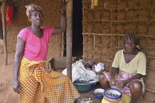 Two women in front of her mud hut, baby lying in a bowl between them, near Kent, Western Peninsula,