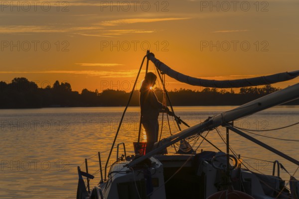 Silhouette of a woman on a sailing boat at sunset with orange sky, Lake Ilinsk, Jelonek, Milomlyn,